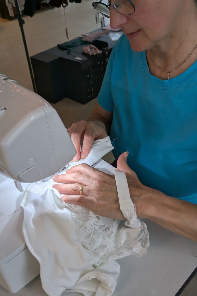 Die Frau näht an einer Nähmaschine ihr eigenes Bralette aus Spitze und Tencel in weiss